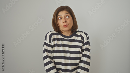 A middle-aged hispanic woman in a striped sweater poses with a quizzical expression against an isolated white wall. © Krakenimages.com