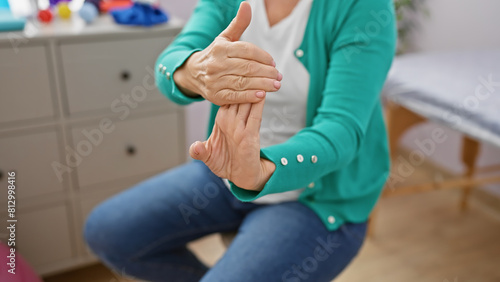 A mature blonde woman stretching her fingers indoors at a rehab clinic, symbolizing hand therapy and recovery. photo