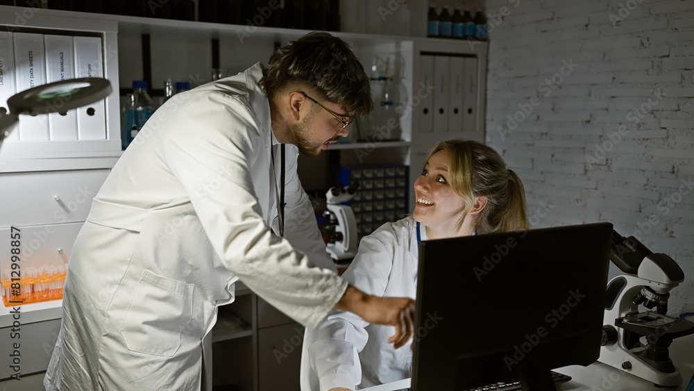 Naklejka premium Two scientists, a man and a woman, collaborate in a laboratory, discussing results in front of a computer.