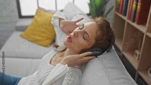 A relaxed young woman enjoying music with headphones while lying on a couch in a cozy living room.