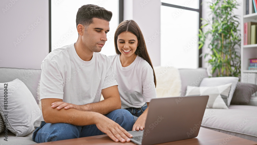 A smiling couple using a laptop together on a couch in a cozy living room. A smiling couple using a laptop together on a couch in a cozy living room.