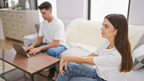 A woman and man in a living room, with the woman looking aside and the man focused on a laptop.