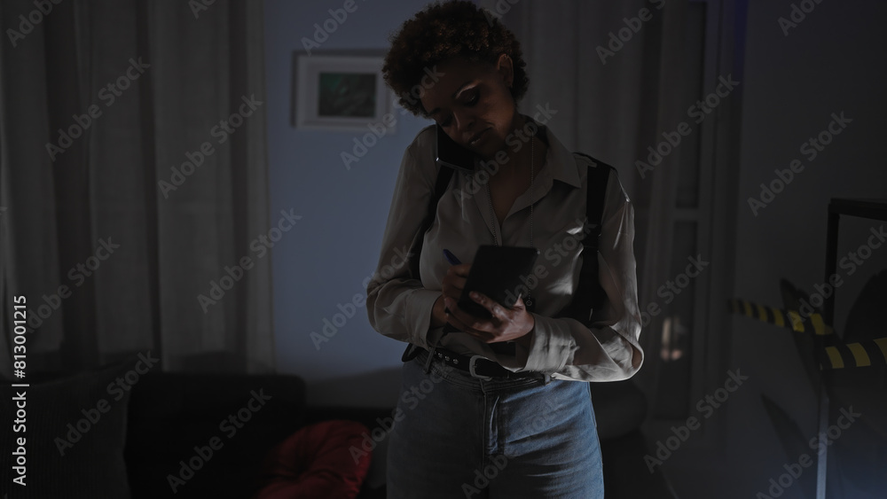 African american woman taking notes during a phone call in a dimly lit indoor crime scene