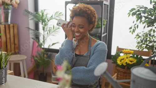 An african american woman smiles while listening to a voicemail indoors at a flower shop.