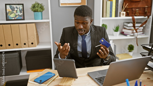 Fotografia African businessman holding credit card looking perplexed in office