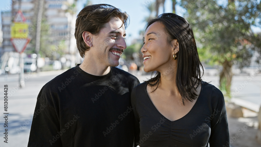 Interracial couple embracing happiness on a sunny urban street with woman and man smiling.