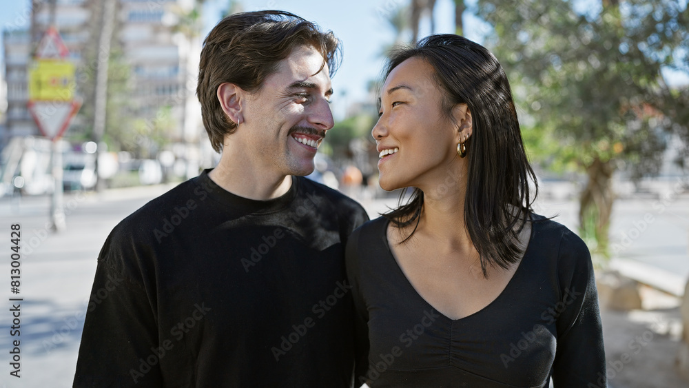 Interracial couple embracing happiness on a sunny urban street with woman and man smiling. Interracial couple embracing happiness on a sunny urban street with woman and man smiling.