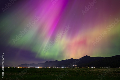 Radiant beams of green and purple light dance across the night sky above a Mountain Range © peteleclerc