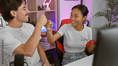 Cheerful interracial couple fist-bumping in a neon-lit gaming room at night, displaying joy and togetherness. photo