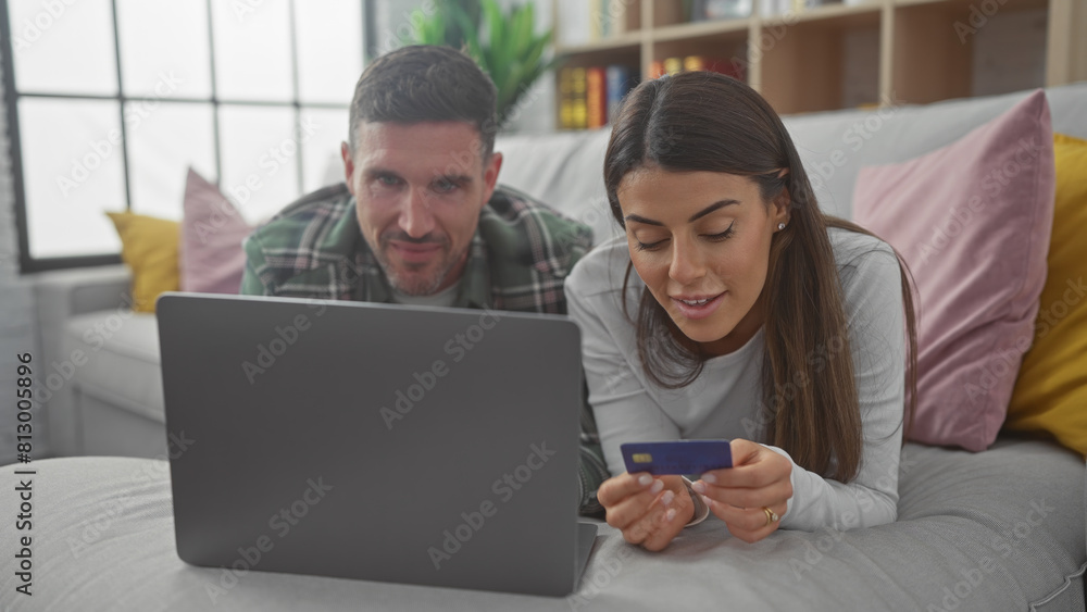 Obraz premium Couple shopping online together on a laptop in their cozy living room with the woman holding a credit card