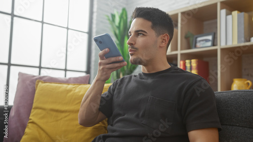 Young hispanic man listening to a voicemail indoors at a cozy home setting with modern decor. photo