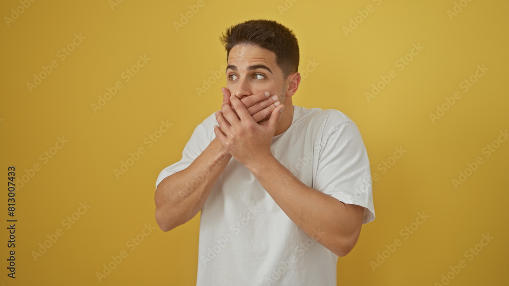 Shocked young hispanic man covering mouth against a vibrant yellow background, portraying silence and surprise. Shocked young hispanic man covering mouth against a vibrant yellow background, portraying silence and surprise.