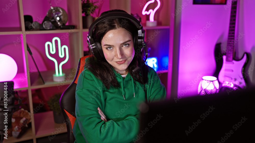 A young caucasian woman with folded arms wearing headphones in a neon-lit gaming room at night A young caucasian woman with folded arms wearing headphones in a neon-lit gaming room at night