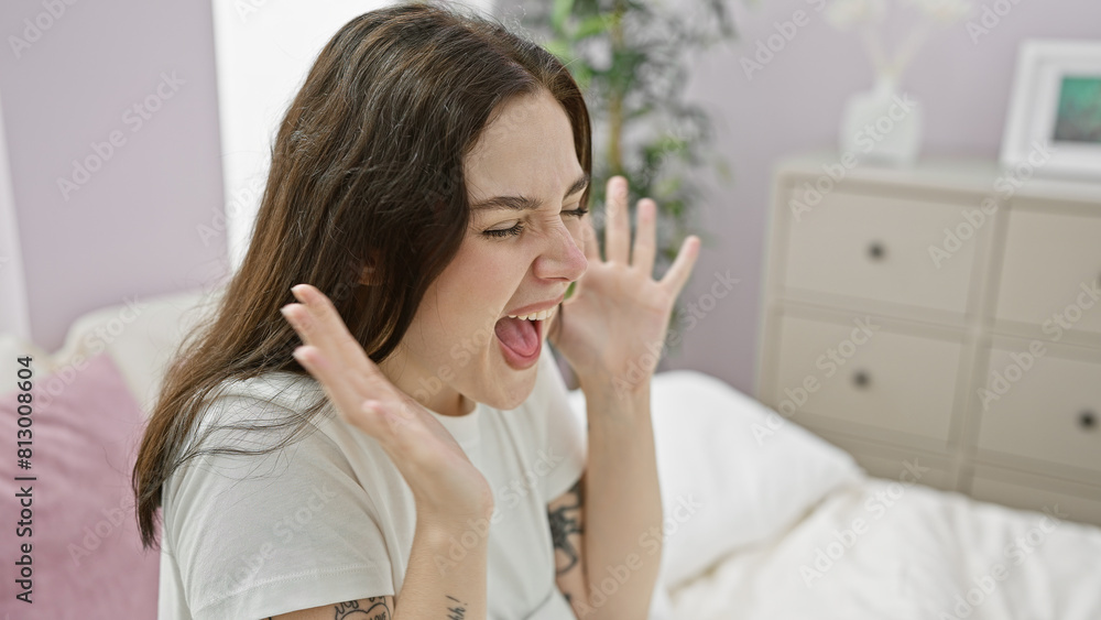 Smiling young woman expressing excitement indoors, with a cozy bedroom background. Smiling young woman expressing excitement indoors, with a cozy bedroom background.