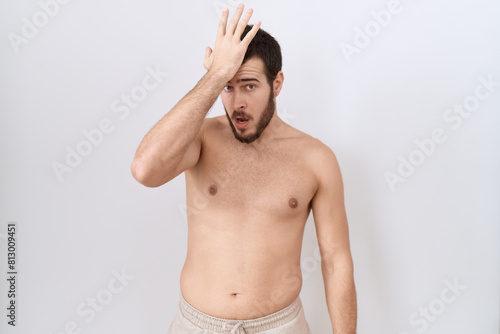 Young hispanic man standing shirtless over white background surprised with hand on head for mistake, remember error. forgot, bad memory concept.