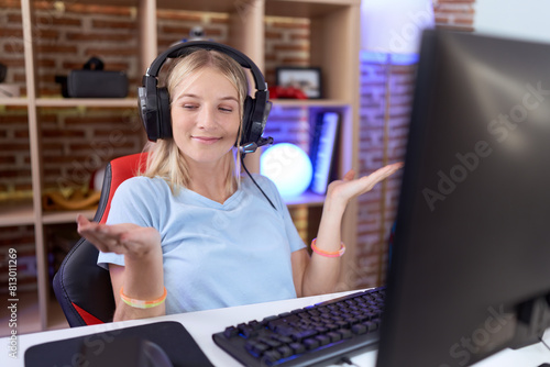 Young caucasian woman playing video games wearing headphones smiling showing both hands open palms, presenting and advertising comparison and balance