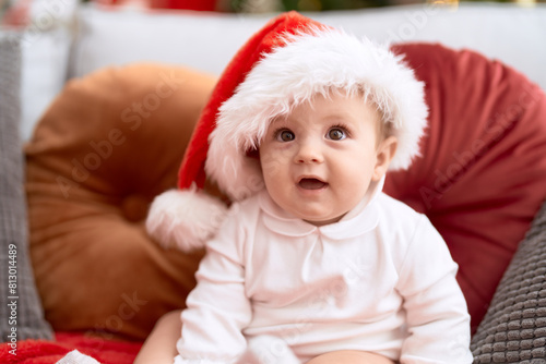 Adorable toddler wearing christmas hat sitting on sofa at home