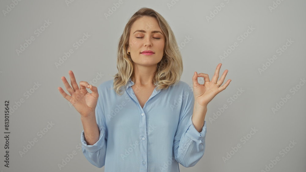 A serene blonde woman meditates in a blue shirt against a white backdrop, emanating calmness and balance. A serene blonde woman meditates in a blue shirt against a white backdrop, emanating calmness and balance.