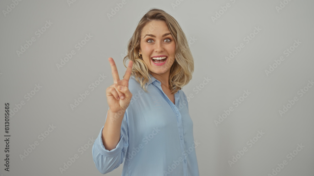 A young, attractive, blonde woman in a blue shirt flashes a peace sign, radiating positivity against a white background. A young, attractive, blonde woman in a blue shirt flashes a peace sign, radiating positivity against a white background.