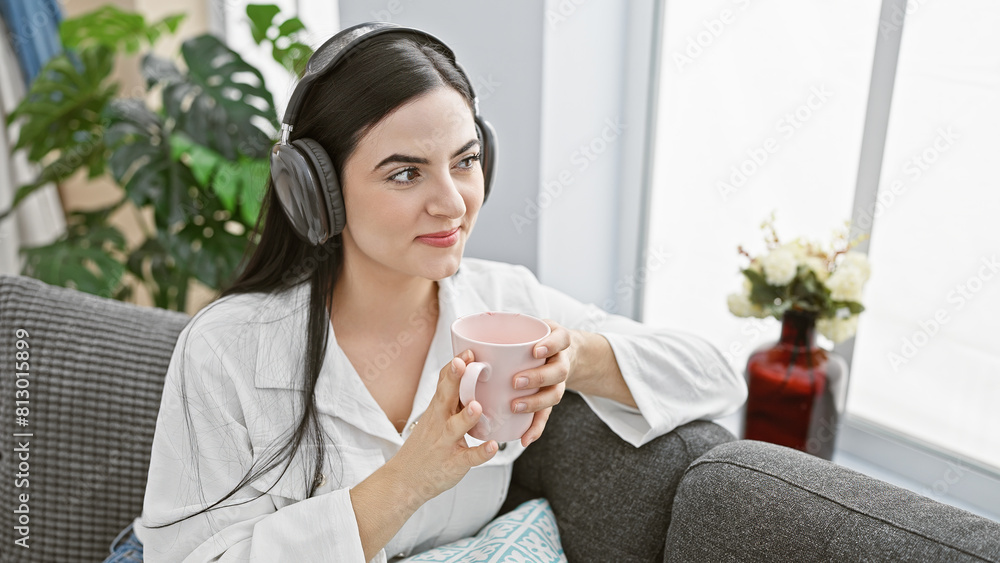 Relaxed hispanic woman with headphones enjoying coffee in a modern living room. Relaxed hispanic woman with headphones enjoying coffee in a modern living room.