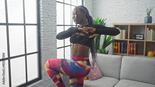 Photography African american woman with braids exercising in a living room, wearing colorful leggings and a black top