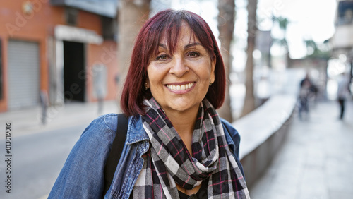 Confident middle-aged hispanic woman smiling in a city street, portraying everyday urban life.