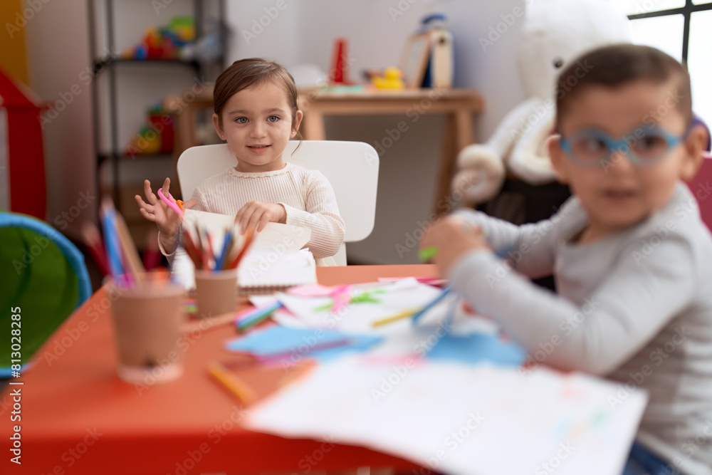 Adorable girl and boy sitting on table cutting paper at kindergarten Adorable girl and boy sitting on table cutting paper at kindergarten
