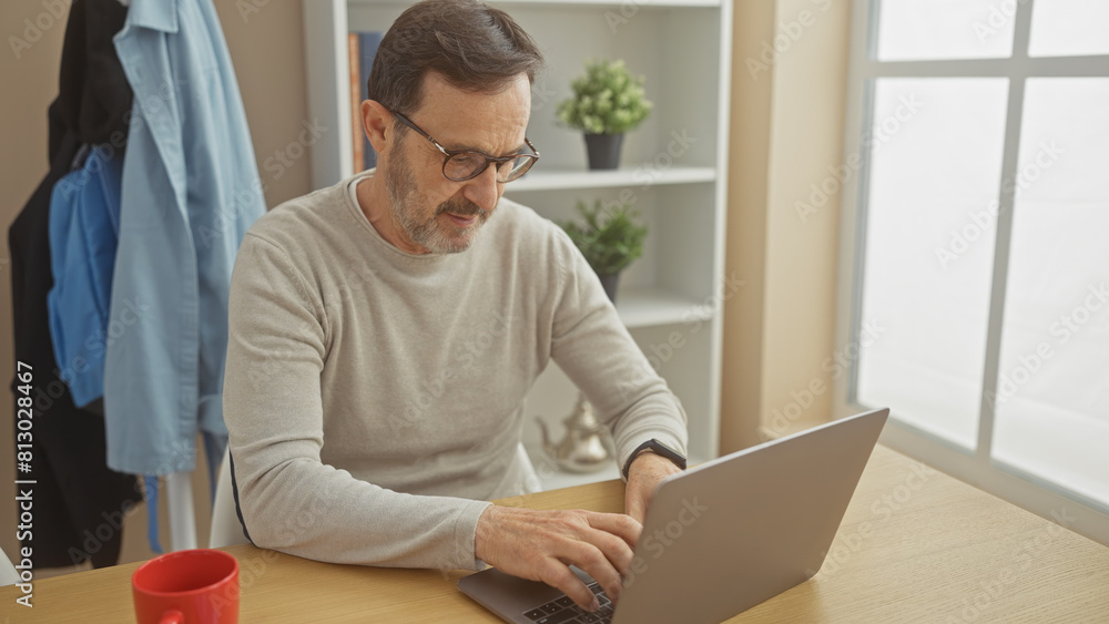 A mature man with a beard works on a laptop in a bright home interior, symbolizing remote work or online communication. A mature man with a beard works on a laptop in a bright home interior, symbolizing remote work or online communication.
