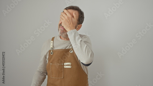 A middle-aged man in a brown apron covers his face against a white background, expressing frustration or fatigue.