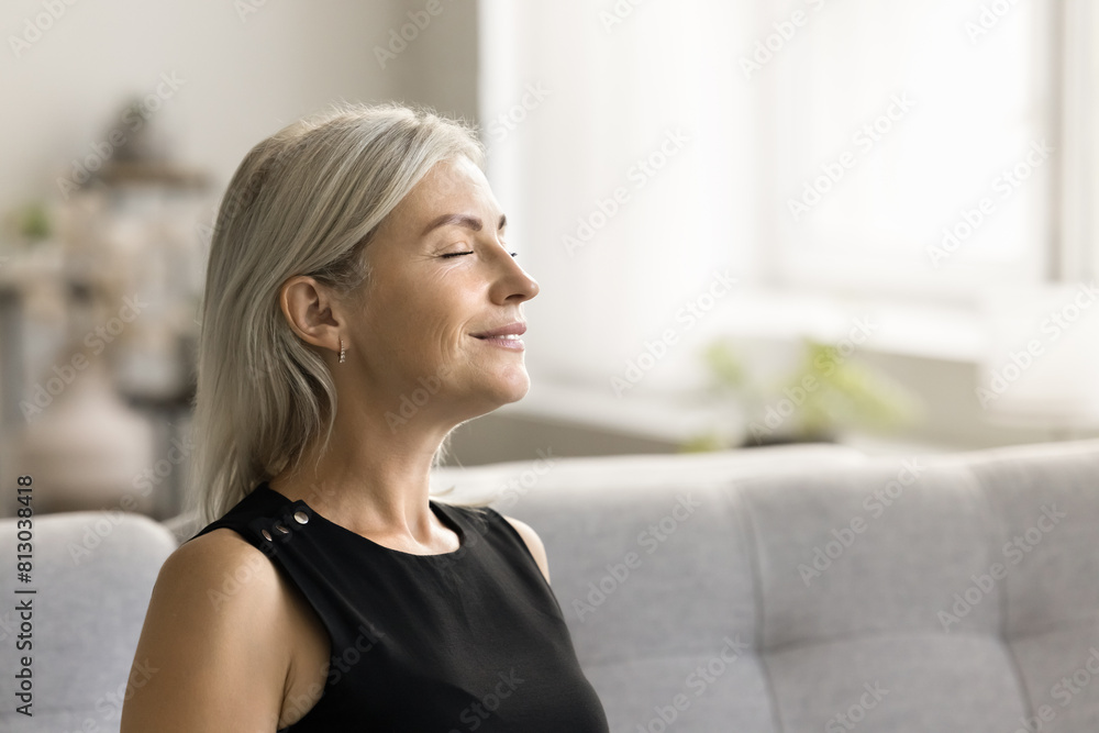 Happy relaxed mature woman enjoying fresh air, smells, relaxation, leisure at home, taking deep breath with closed eyes, smiling, meditating, reloading mind, enjoying stress relief technique Happy relaxed mature woman enjoying fresh air, smells, relaxation, leisure at home, taking deep breath with closed eyes, smiling, meditating, reloading mind, enjoying stress relief technique