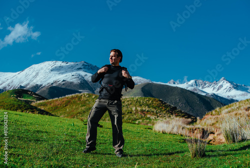 Man hiker with backpack stands in picturesque valley on mountains background