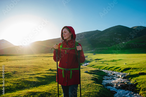 Young woman tourist standing by stream in picturesque mountain valley on a sunny day