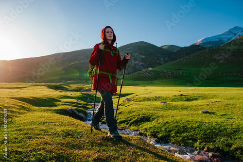 Young woman tourist walks along stream in picturesque mountain valley on a sunny day