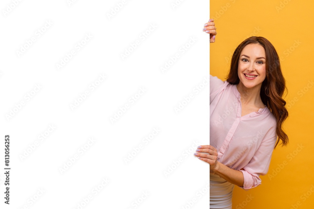A woman is cheerfully posing while holding a white board in front of her, displaying a joyful expression. She appears content and confident as she holds the board firmly and smiles towards the camera. A woman is cheerfully posing while holding a white board in front of her, displaying a joyful expression. She appears content and confident as she holds the board firmly and smiles towards the camera.