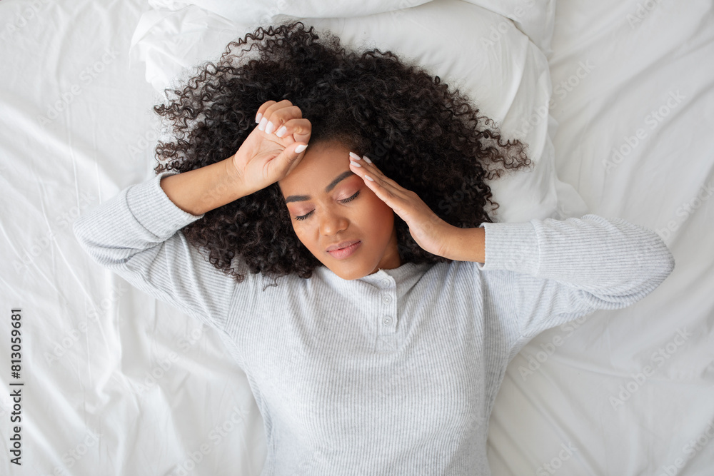 Hispanic woman is laying down in bed with her head resting in her hands, appearing contemplative or deep in thought, top view Hispanic woman is laying down in bed with her head resting in her hands, appearing contemplative or deep in thought, top view