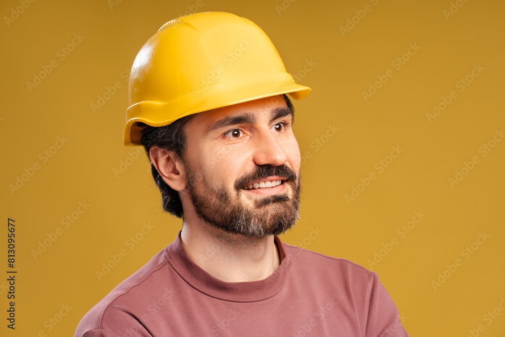 Young workman with helmet posing in studio, looking to the side, isolated on yellow