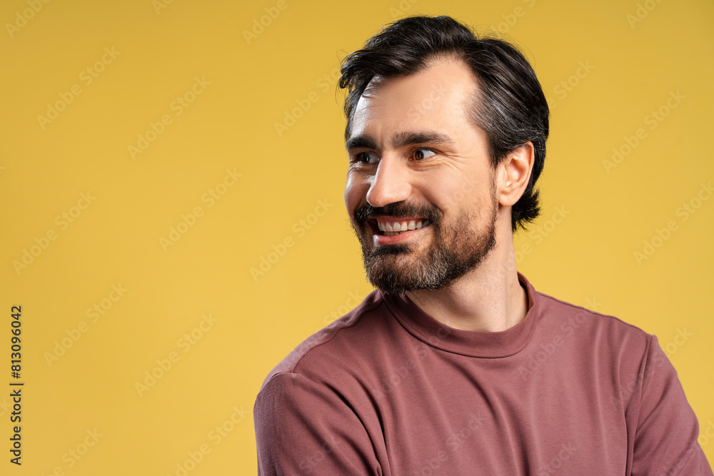 Obraz premium Happy bearded young man posing in studio looking to the side. Isolated on yellow