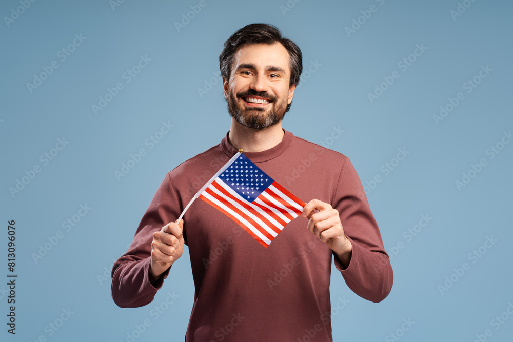 Happy young man showing national flag of United States, posing in studio, isolated on blue