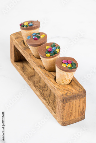 Dessert waffle cornet with chocolate nut cream and colored dragees. On a wooden serving stand