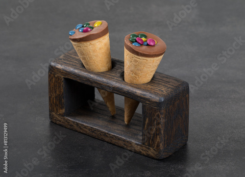 Two mini waffle cornets, with chocolate nut cream and colored dragees. On a wooden serving stand. White background. Close up