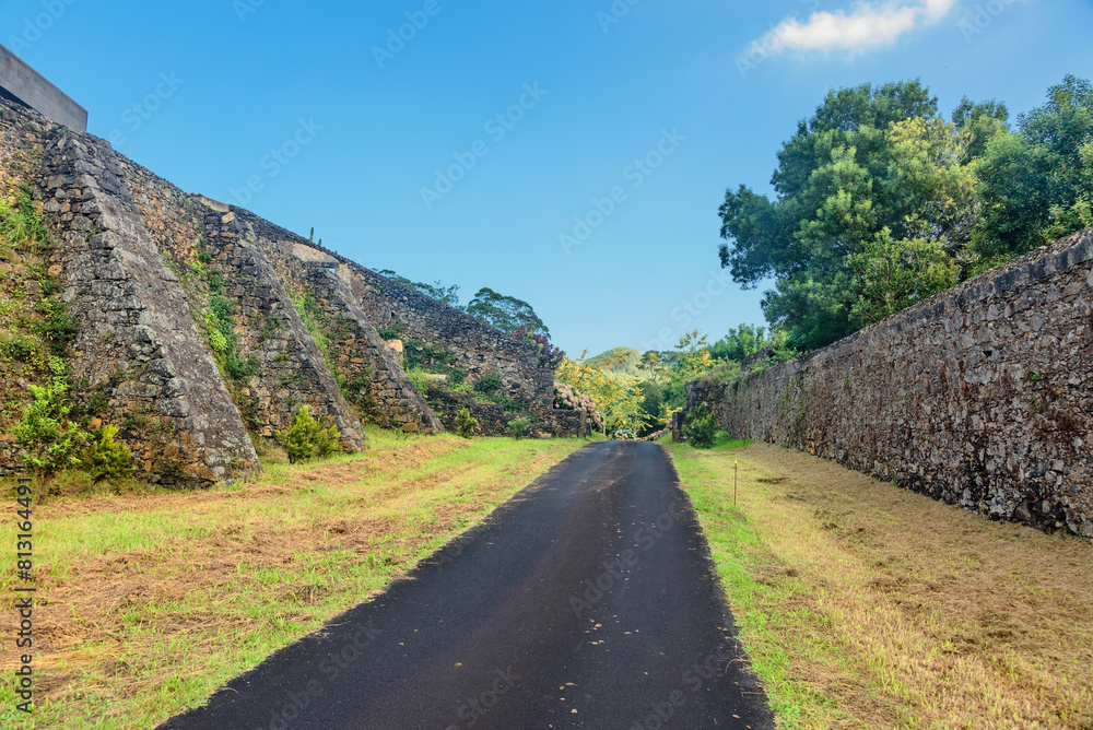 Road in a field between stone walls under a blue sky. Sao Miguel island, Portugal