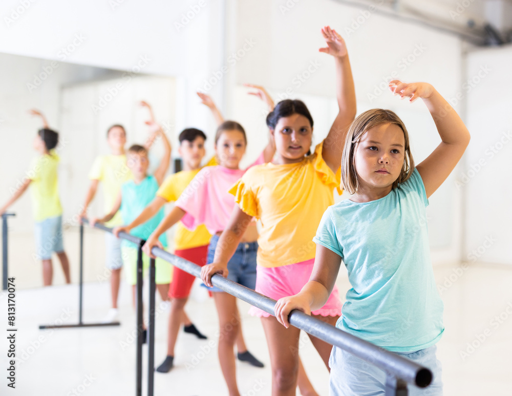 Fototapeta premium Portrait of focused tween girl practicing ballet positions near bar during group class in dance school.