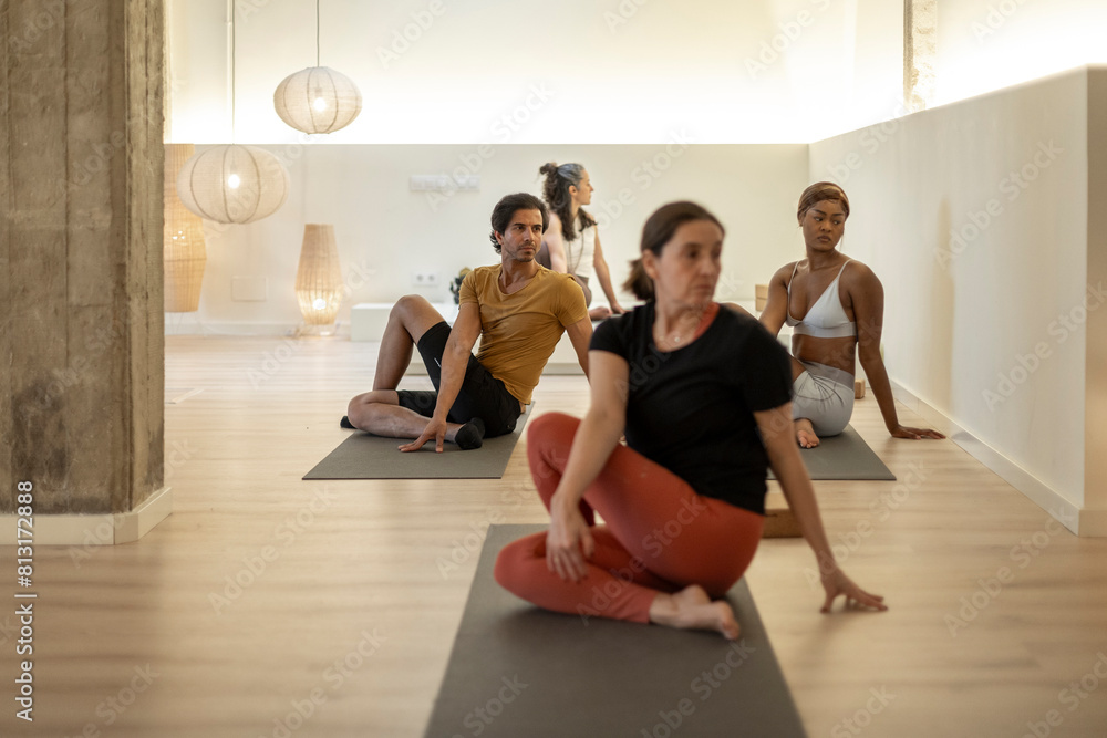 Fototapeta premium Diverse yoga class in seated twist pose with instructor leading in studio.