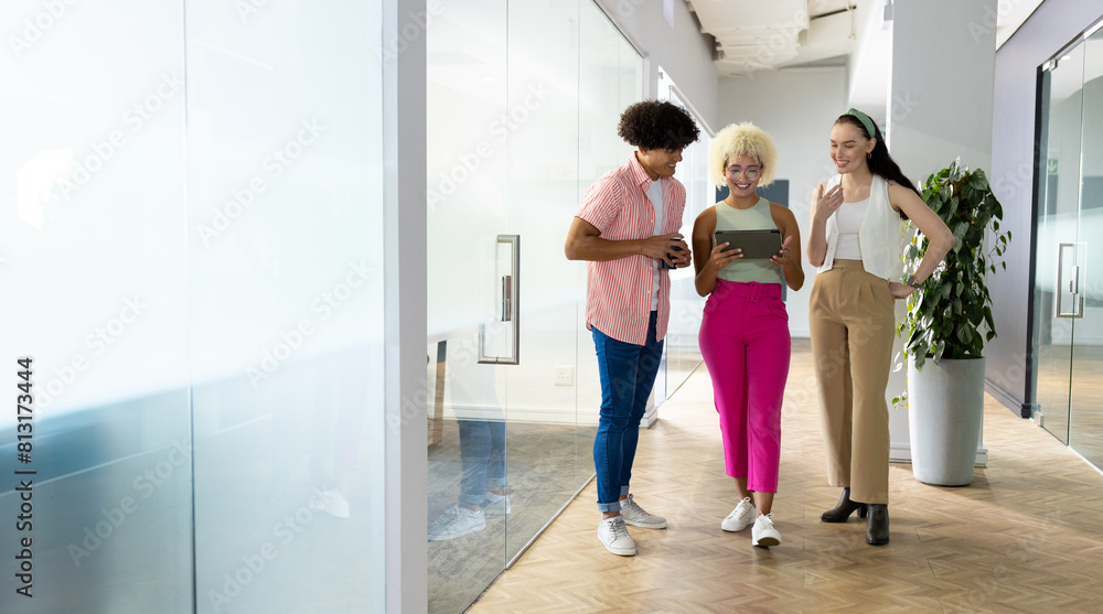 In modern office, diverse young team sharing content on tablet, walking, copy space In modern office, diverse young team sharing content on tablet, walking, copy space