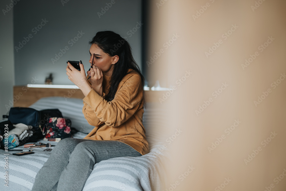 A young adult woman sits on a bed, focusing intently as she applies makeup, her personal items scattered around. A young adult woman sits on a bed, focusing intently as she applies makeup, her personal items scattered around.
