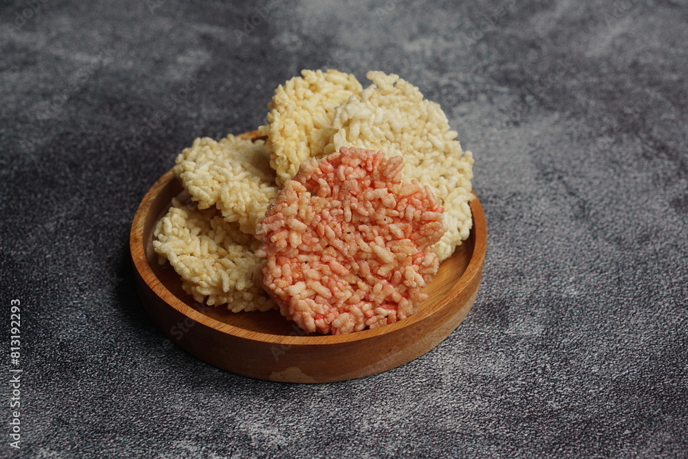 Rengginang is a typical Indonesian snack made from glutinous rice grains that are seasoned and fried. Served on a wooden table on black background. Indonesian food. Camilan gurih. Rengginang is a typical Indonesian snack made from glutinous rice grains that are seasoned and fried. Served on a wooden table on black background. Indonesian food. Camilan gurih.