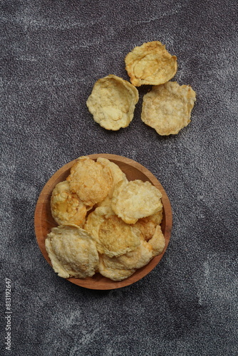 Emping, Indonesian traditional snack made from melinjo or belinjo seeds. Bitter and savory. served on wooden plate with black background photo