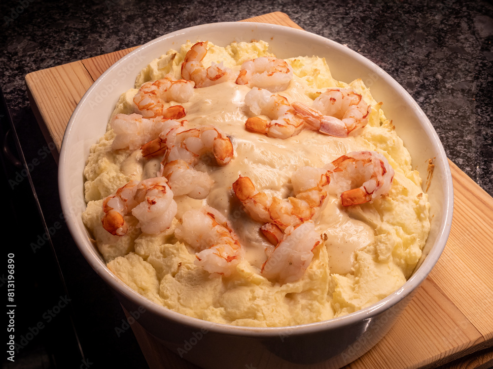 Seafood dinner in a white casserole dish with mashed potatoes, giant shrimps, white wine sauce and mashed potatoes, served on a wooden board. Seafood dinner in a white casserole dish with mashed potatoes, giant shrimps, white wine sauce and mashed potatoes, served on a wooden board.