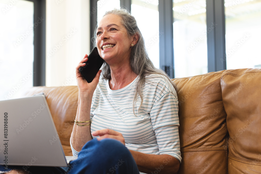 At home, Caucasian mature woman talking on smartphone, sitting with laptop At home, Caucasian mature woman talking on smartphone, sitting with laptop