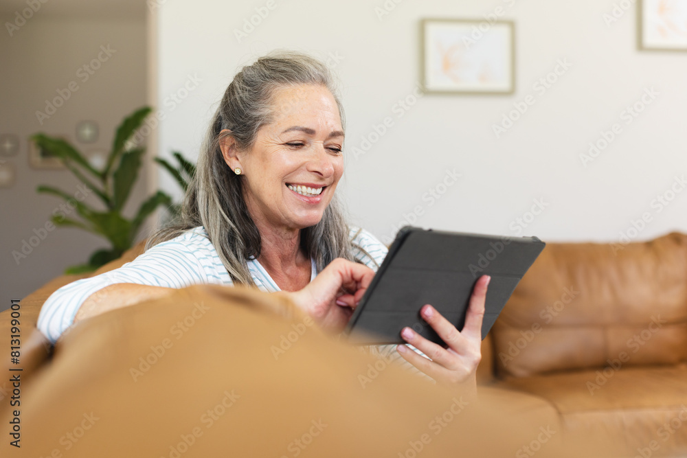 At home, mature Caucasian woman holding a tablet, laughing At home, mature Caucasian woman holding a tablet, laughing